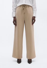 Beežid laia lõikega püksid nöörvöökohaga ja pehme tekstuuriga. Sobitatud pruunide teravate kontsadega, et luua kontrast. Ülasel on vertikaalsed triibud.