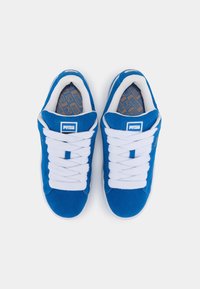 Paire de baskets bleues Puma avec lacets blancs vue de dessus sur un fond blanc uni.