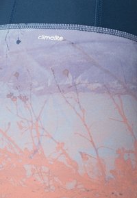 Legging avec un dégradé de bleu et de pêche. Le tissu est extensible, avec une texture lisse et des motifs floraux imprimés.