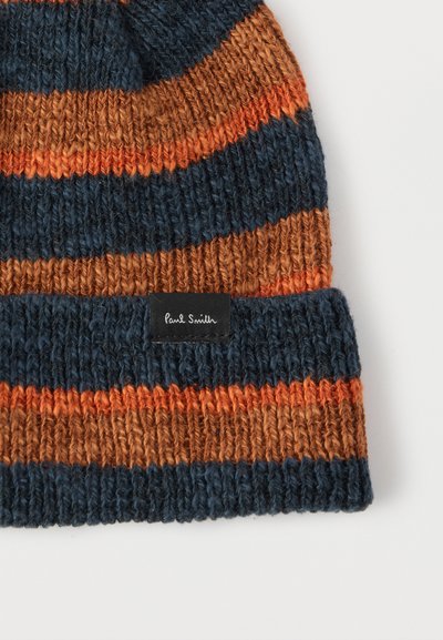 Πλεκτός σκούφος σε σκούρο μπλε, σκουριασμένο πορτοκαλί και πορτοκαλί ρίγες. Διαθέτει ρεβέρ με μαύρη ετικέτα που αναγράφει "Paul Smith." Υφή από νήμα.