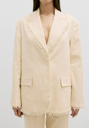 Beige blazer met rafelige randen, notch revers, twee voorzakken, gladde textuur, op maat gemaakt, met een diepe V-hals.