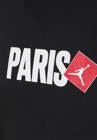 Camiseta de algodón negra con gran texto blanco "PARIS" y un logo de diamante rojo con una figura de salto en blanco.