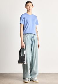 Svetlo modra bombažna majica z rahlo sproščenim krojem; izprane široke kavbojke z robovi; sijoča črna torbica; sive superge s kremnimi poudarki.