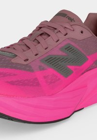 Close-up af en pink og lilla New Balance løbesko med en tyk sål, mesh-overdel og snørebånd bundet foran.