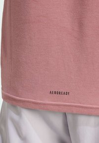 T-shirt en coton rose avec des manches courtes et un ourlet droit, affichant un logo « AEROREADY » noir près du bas.