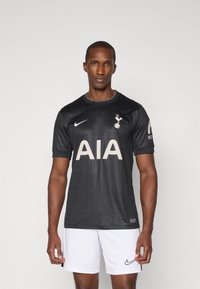 Maglietta da calcio nera a maniche corte, con motivo a griglia, grande logo "AIA" in beige chiaro, logo Nike sul petto, indossata con pantaloni corti bianchi.