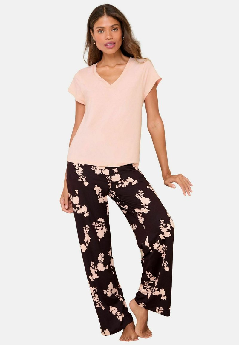 Set de pijama format dintr-un top scurt cu mânecă scurtă, de culoare roz deschis, și pantaloni negri cu un model floral în nuanțe delicate de roz.