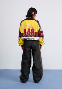 Sweatshirt de ciclismo oversized multicolorido com gráficos ousados, incluindo "Cyclone 948", combinado com calças de denim pretas de perna larga com listras brancas.
