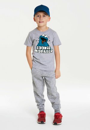 Gray short-sleeve t-shirt featuring a Cookie Monster graphic with blue accents. Paired with gray sweatpants and red athletic shoes.