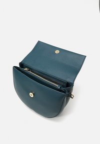 Tyrkysová kožená taška s hladkým povrchem, zaobleným tvarem a zlatým zapínáním na patentku. Má přední zipovou kapsu a dvě vnitřní přihrádky.