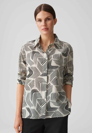 Camicia a bottoni con sfondo beige e linee nere ondulate e motivi geometrici. Maniche corte ripiegate, trama di tessuto morbida.