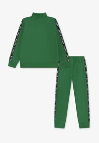Conjunto de chándal verde que incluye una chaqueta con cremallera y cuello alto, con acentos de rayas negras, y pantalones a juego con cintura elástica y puños.