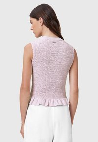 Ljust rosa ärmlös topp med smockad struktur och volangkant. Slätt tyg, minimalistisk design och subtil märkning på baksidan.