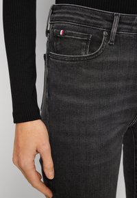 Jeans de mezclilla negra con un corte ajustado, que cuentan con un bolsillo delantero, costuras blancas y un pequeño acento en rojo, blanco y azul en el bolsillo trasero.