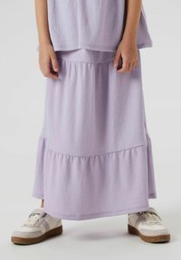 Ensemble lilas en deux pièces comprenant un haut texturé et une jupe à volants. La jupe a un ourlet froncé, associée à des baskets blanches.