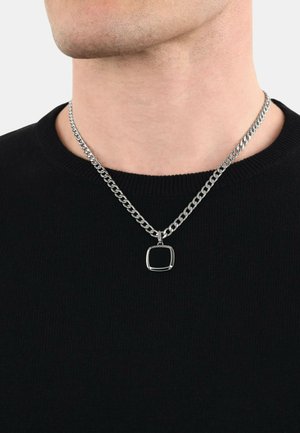 Silver chain necklace with a square pendant featuring a black inlay, worn over a black sweater. Chain has a smooth, polished texture.