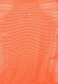 Maglietta sportiva Nike arancione con un motivo testurizzato e logo riflettente. Tessuto liscio e leggero che presenta linee orizzontali e punti sottili.