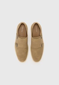 Des chaussures à enfiler beiges en daim, dotées d'un design à double boucle et d'une semelle en caoutchouc claire. Texture lisse avec un minimum de détail.