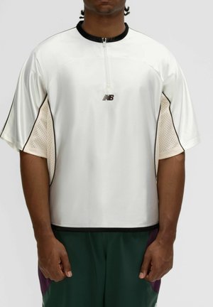 Homme portant un t-shirt de sport blanc à manches courtes avec un col noir et une fermeture éclair, avec un petit logo New Balance noir sur la poitrine.
