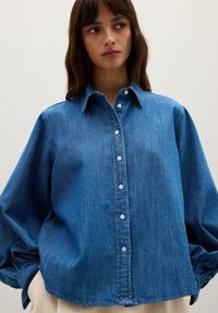 Blue denim shirt with a button-down front, long sleeves, and a relaxed fit. Features a classic collar and slight texture.