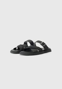 Black sandals featuring woven straps, a flat sole, and an adjustable buckle. Made from synthetic materials with a smooth texture.