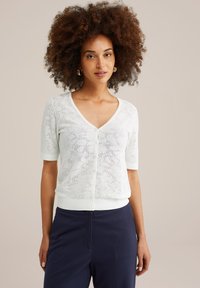 Cardigan blanc à manches courtes avec un motif en dentelle, col en V et fermeture à boutons. Les poignets et la taille côtelés ajoutent de la texture au design.
