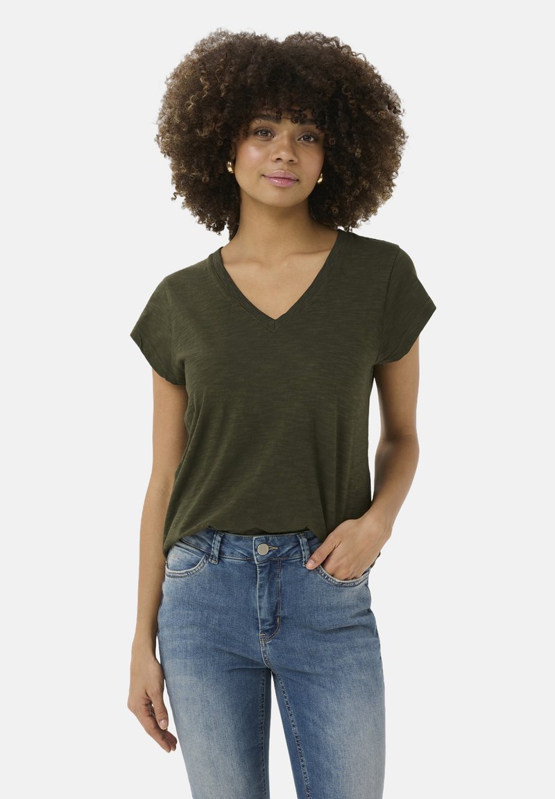 Alyvos žalios V formos apykaklės marškinėliai su trumpomis rankovėmis, pagaminti iš minkštos medžiagos. Dėvimi su išblukusiomis mėlynomis džinsomis, turinčiomis laisvą siluetą ir minimalų dizainą.