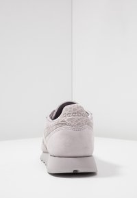 Ljusgrå mocka sneakers med snördetaljering, rund tå, vadderad krage och platt gummisula. "Reebok"-logotyp präglad på baksidan.