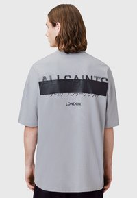 T-shirt oversize gris clair avec texte en bloc noir. Comprend "ALLSAINTS" et "LONDRES" en impression en relief. Tissu doux, manches courtes.