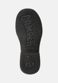 Suela de zapato de goma negra con textura acanalada, que presenta la marca “CAMPER” y la impresión de talla “42”, exhibida sobre un fondo liso.