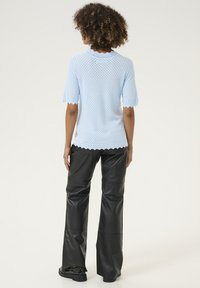 Šviesiai mėlynas nertinis trumpomis rankovėmis su banguota apykakle ir kraštais, derinamas su aukštu liemeniu, juodais odiniais plačiomis kelnėmis.