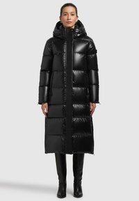 Must pufferjakk kapuutsiga, mille läikiv, tikitud viimistlus ja pikad varrukad. Sellel on kaks küljetaskut ja põlveni ulatuv disain.