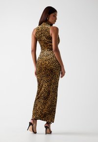 Sukienka maxi w panterkę, dopasowana, wykonana z welwetowej tkaniny. Wysoki dekolt, bez rękawów, o sylwetce podkreślającej ciało. Zestawiona z czarnymi sandałami na obcasie.