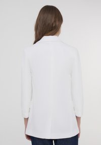 Biała marynarka o dopasowanym kroju, z długimi rękawami podwiniętymi przy mankietach, gładką fakturą i pojedynczym rozcięciem z tyłu.