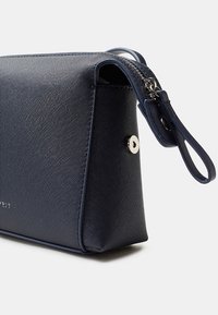 Piccolo portamonete texturizzato di colore blu navy con chiusura a zip e manico ad anello su sfondo bianco.