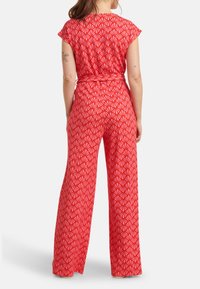 Rode jumpsuit met korte mouwen, voorzien van een geometrisch wit patroon, een gestrikte taille en een brede pijpdesign. Soepele stof met een ontspannen pasvorm.
