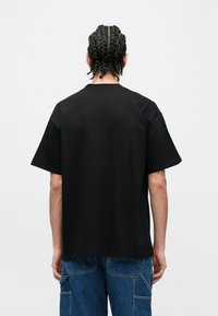 Svart t-skjorte med korte ermer, rund hals og avslappet passform. Laget av mykt stoff, med minimal søm og uten synlige logoer.