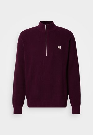 Purple knit sweater with a high collar and quarter-zip, featuring a small logo patch on the left chest and ribbed cuffs.