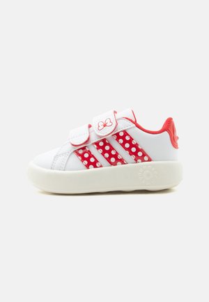 Witte kindersneaker met rode polkadotstrepen, rode bies, twee klittenbandsluitingen en een rood vlinderlogo op een witte zool.