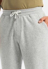 Helle graue Jogginghose mit einem elastischen Bund, verstellbarem weißen Kordelzug, Seitentaschen und einer weichen, gerauten Textur.