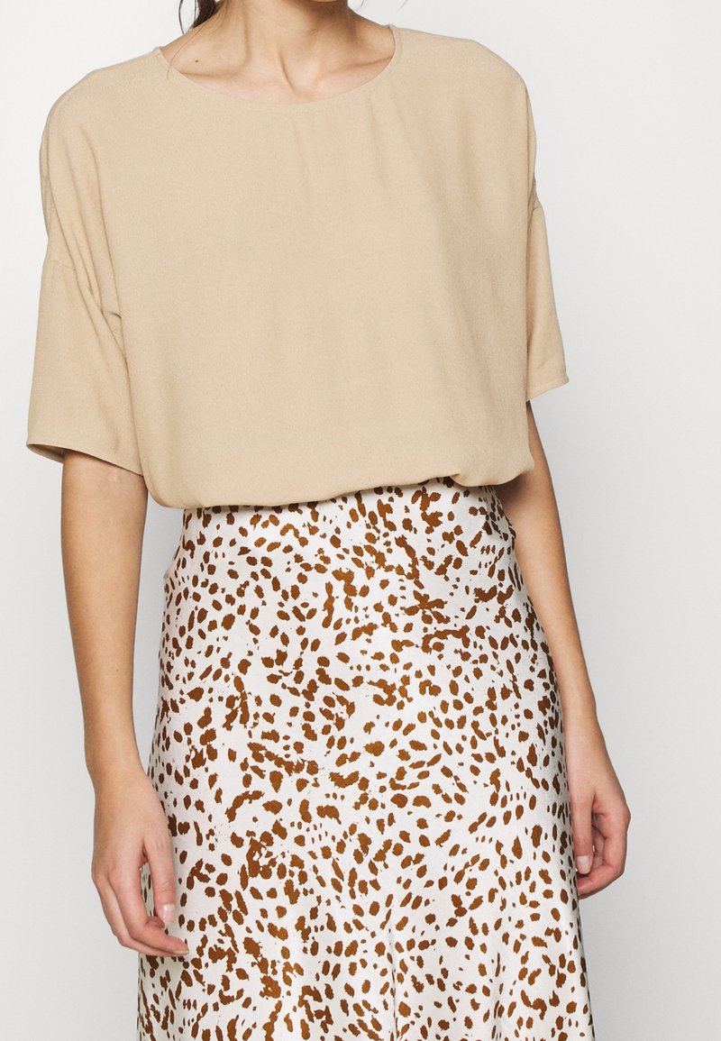 Beige kortärmad topp gjord av mjukt tyg, tillsammans med en mönstrad kjol med vit botten och spridda bruna fläckar.