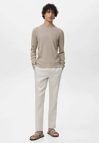 Maglione a coste beige chiaro, pantaloni crema e sandali con cinturino marroni. Il maglione è attillato, mentre i pantaloni hanno una gamba affusolata con una texture morbida.