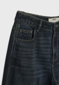 Tmavě modré džíny z denimu s středním pasem, designem s pěti kapsami, kontrastním švem a jedním knoflíkem na zavírání pasu.