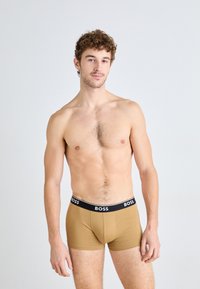 Braune Boxershorts mit einem schwarzen Bund, auf dem die Marke "BOSS" in weißem Schriftzug zu sehen ist. Der Stoff wirkt glatt, eng anliegend und flexibel.