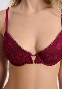 Burgunderfarbenes Spitzen-BH mit dreieckigem Design, strukturiertem Blumenmuster, verstellbaren Trägern und einem zentralen goldenen Ringakzent.