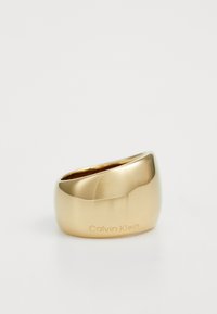 Goldfarbener Metallring mit einem glatten, abgerundeten Design und einer dezenten Gravur von "Calvin Klein" auf einer Seite.