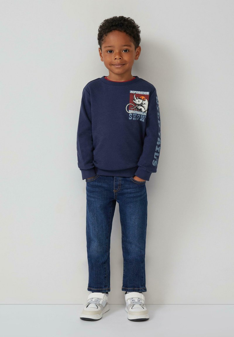 Felpa navy con stampa grafica e testo sulla parte anteriore, abbinata a jeans blu e sneakers bianche con accenti grigi. Texture liscia.