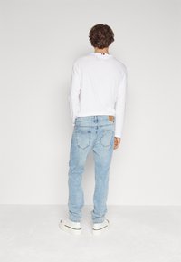 Los jeans de mezclilla azul claro tienen un ajuste relajado con dos bolsillos traseros, combinados con una camisa blanca de manga larga y zapatillas blancas.