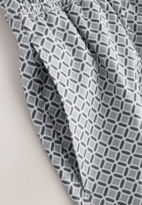 Gray fabric with a white and dark gray geometric hexagon pattern, showing gathered elastic and a side seam with stitching details.