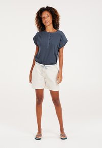 Marineblauwe top met korte mouwen en knopenlijst, gecombineerd met crèmekleurige shorts en een lichtblauwe trekkoord. Gekozen voor donkere flip-flops.
